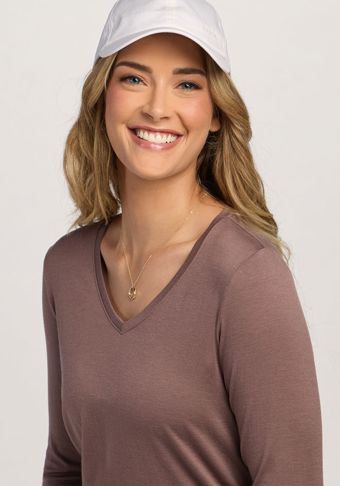 Smiling woman in a white cap and Woolx Millie Long Sleeve - Peppercorn, gold necklace, on a light background.