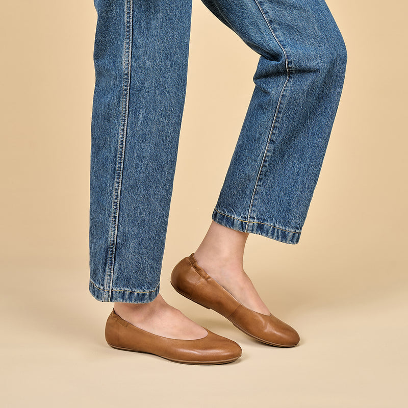A closeup of brown ballerina flats shown on foot.