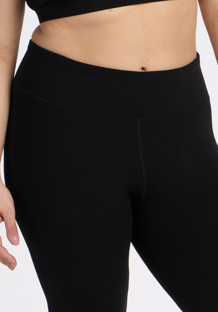 Wearing Woolx’s Morgan Flare Pants in black, paired with a black crop top; shown from midriff to upper thighs, one arm relaxed at the side.