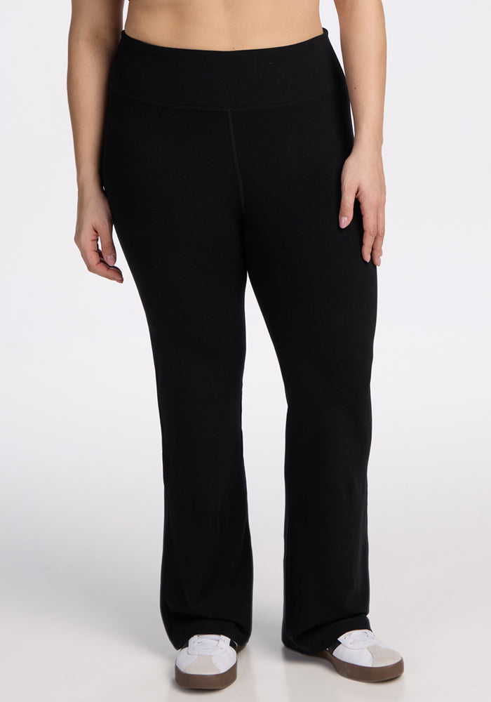 A person models the Woolx Morgan Flare Pants in black with white sneakers, standing against a plain white background. The image is cropped from mid-torso to feet. | Juliana is 5'10", wearing a size XL