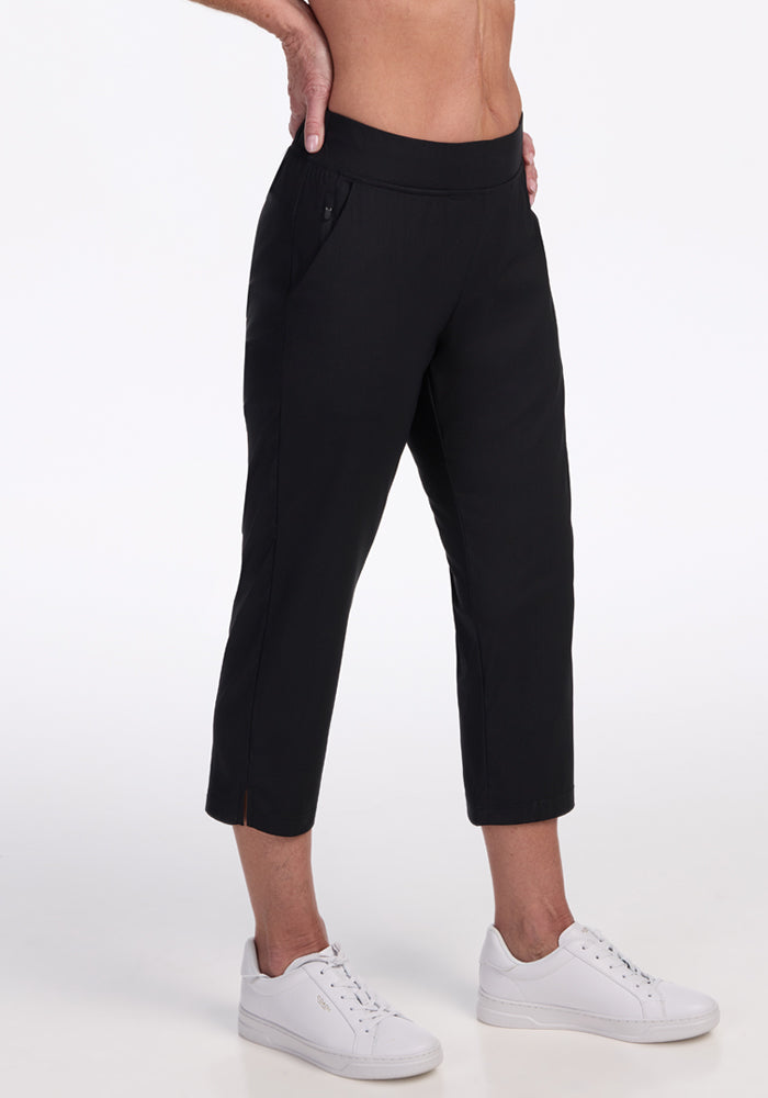 Model wears Woolx Nicole Crop Pants in black, styled with white sneakers. The cropped pants finish above the ankles and feature side pockets, combining comfort and style. Shot against a plain white background, with torso partially visible.