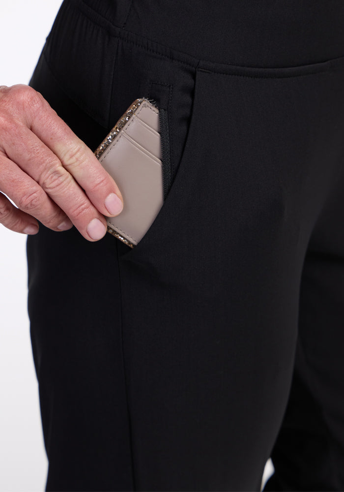 A hand places a beige cardholder into the pocket of Woolx Nicole Crop Pants in black.