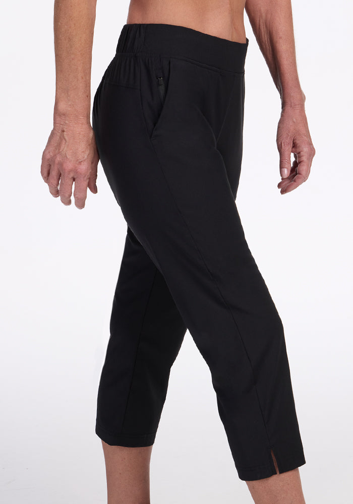 Model showcases Woolx Nicole Crop Pants in black, featuring a cropped length and subtle hem slit; only the lower torso and legs are visible against a white background.