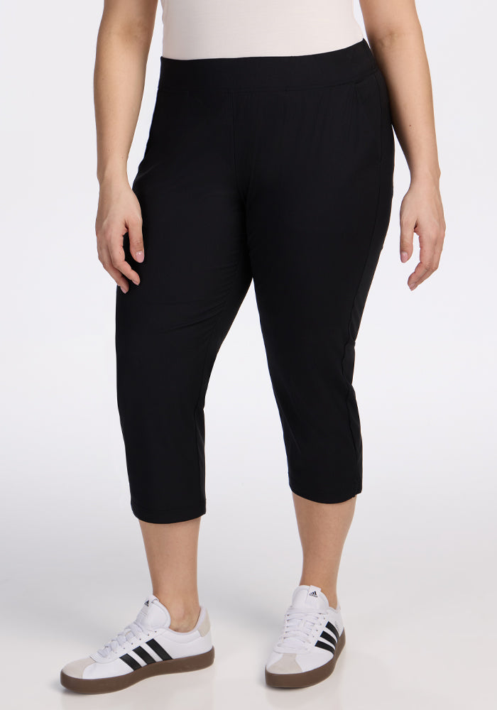 A person wearing Woolx Nicole Crop Pants in black, a white top, and white Adidas sneakers with black stripes stands against a plain white background. | Juliana is 5'10", wearing a size XL