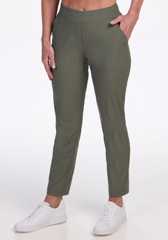 A person wearing Woolx Nicole Petite Ankle Pant in Sage Olive and white sneakers stands against a plain white background with one hand in a pocket.