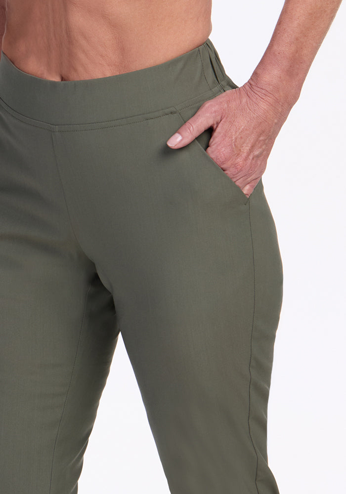 A person models the Woolx Nicole Petite Ankle Pant in Sage Olive, with one hand in their pocket, against a white background. The photo highlights the waist, hips, and upper thighs of these breathable women's pants.