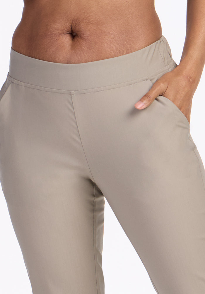 Close-up of a person wearing Woolx Nicole Petite Ankle Pant in Vintage Khaki, featuring a lightweight tapered fit and elastic waistband, with their right hand in the pocket. Photo cropped midriff to mid-thigh on a plain white background.