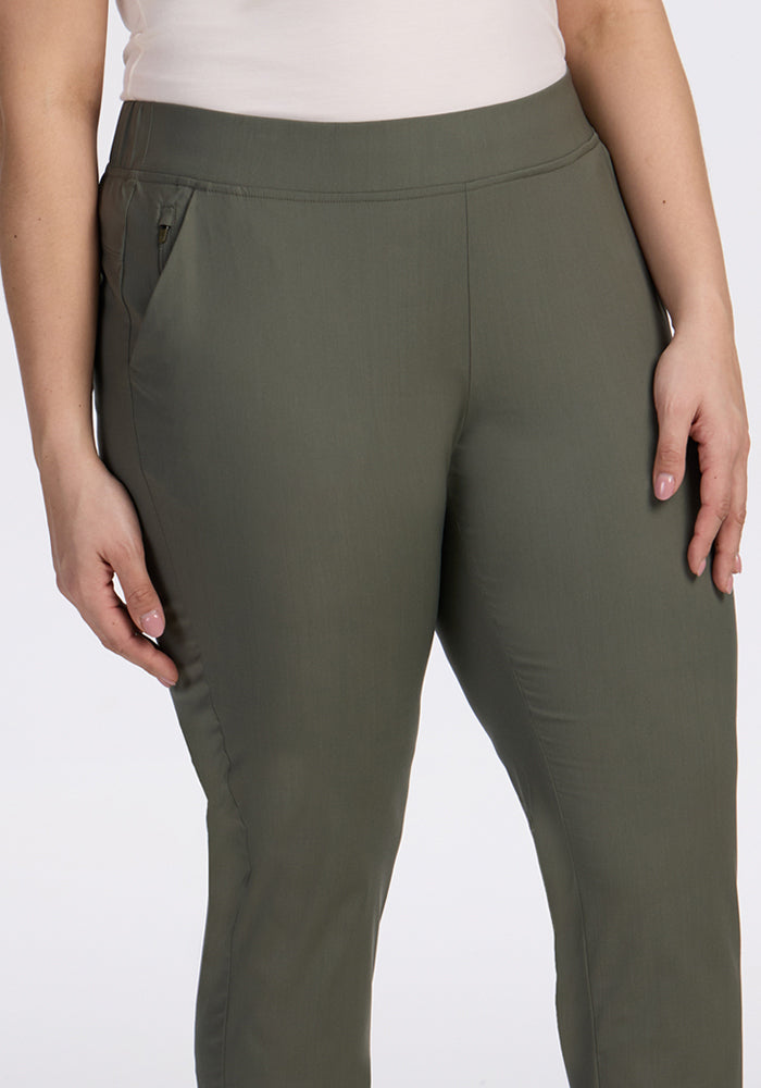 A person wears Woolx Nicole Tall Ankle Pant in Sage Olive—a lightweight, breathable pant with a tapered leg—paired with a white top. The focus is on the lower torso and upper legs, right hand by their side, left near the pocket.