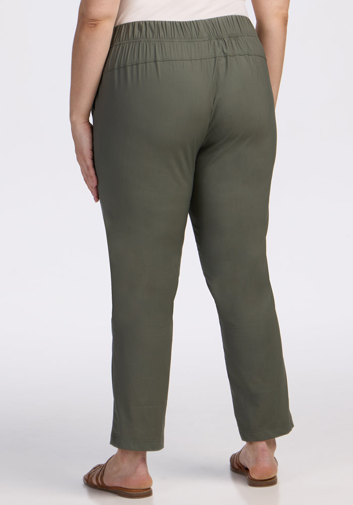 A person is shown from the back, standing against a plain white background, wearing Woolx Nicole Tall Ankle Pant in Sage Olive with brown sandals.