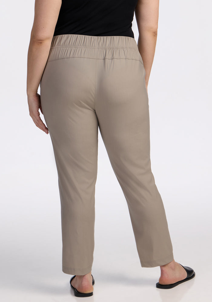 A person wearing Woolx Nicole Tall Ankle Pant in Vintage Khaki, featuring moisture-wicking fabric and an elastic waistband, paired with black flat sandals, is shown from the back against a plain background.