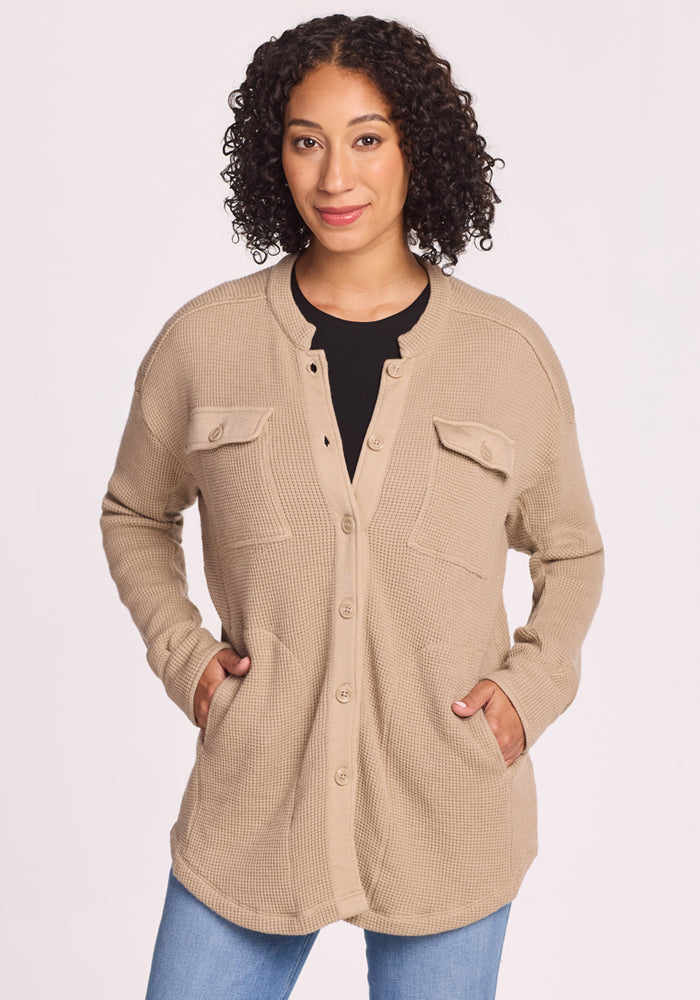A woman with curly hair wears the Woolx Oaklynn Waffle Shacket in Biscotti, featuring two chest pockets, over a black top and blue jeans, standing with her hands in her pockets against a plain light background. | Tori is 5'7", wearing a size S