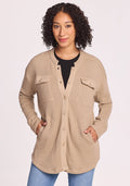 A woman with curly hair wears the Woolx Oaklynn Waffle Shacket in Biscotti, featuring two chest pockets, over a black top and blue jeans, standing with her hands in her pockets against a plain light background. | Tori is 5'7", wearing a size S