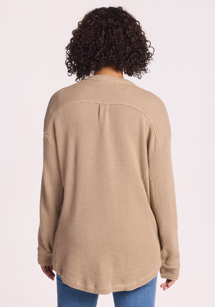 A person with curly hair is seen from behind wearing the Woolx Oaklynn Waffle Shacket in Biscotti and blue jeans, set against a plain light background.