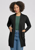 A curly-haired person wears a Woolx Paisley Cardigan in black over a green top and blue jeans. Made from lightweight Merino wool, they stand with hands in the cardigan pockets against a plain background. | Tori is 5'7", wearing a size S
