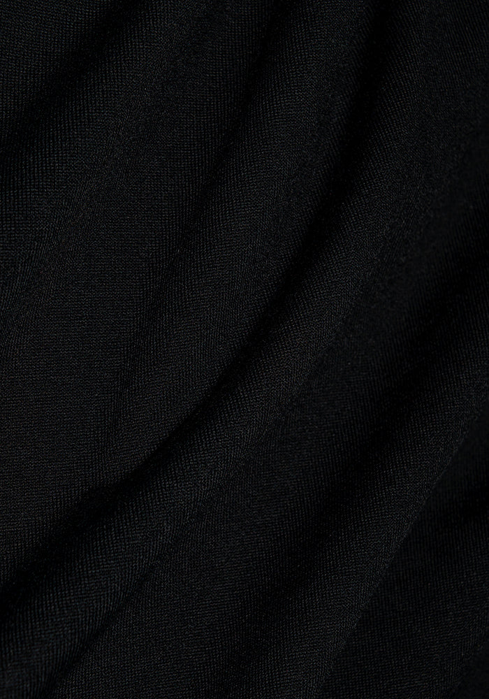The Paisley Cardigan by Woolx features close-up textures of smooth black Merino wool, showcasing soft folds with a subtle wave-like pattern. The fabric appears slightly reflective under light, echoing its lightweight mid-thigh length design.