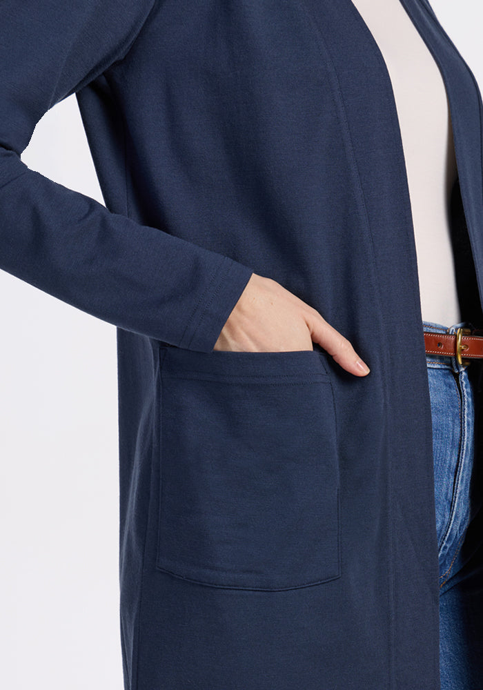 A person wearing a Woolx Paisley Cardigan in Deep Navy with their right hand in the pocket, paired with a white top, blue jeans, and a brown belt. The background is plain white.