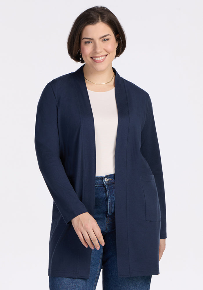 A woman with short brown hair smiles while wearing the Woolx Paisley Cardigan in Deep Navy over a white top and blue jeans, standing against a plain white background. | Juliana is 5'10", wearing a size XL