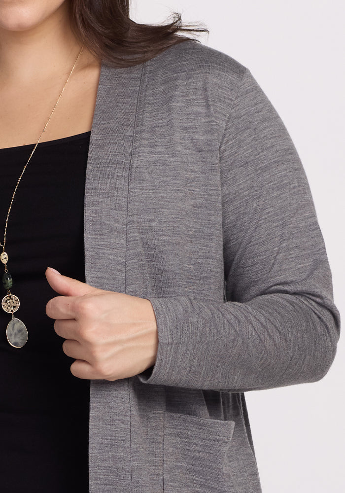 A person in a Woolx Paisley Cardigan - Graphite Heather over a black shirt adjusts the cardigan for feather-light comfort. A long necklace with a pendant complements their look, exuding the elegance of women's essentials against a plain white background.