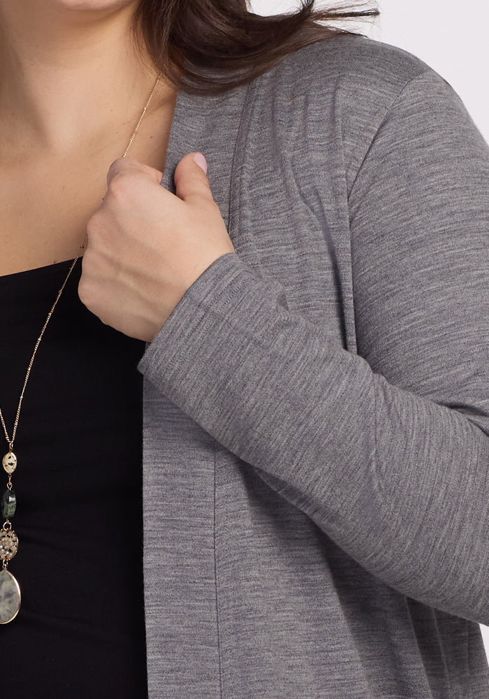 A person wearing a Woolx Paisley Cardigan in Graphite Heather over a black top holds the garment near the shoulder. They sport a long necklace with a pendant, and their partially visible hair accentuates essential style with feather-light comfort.