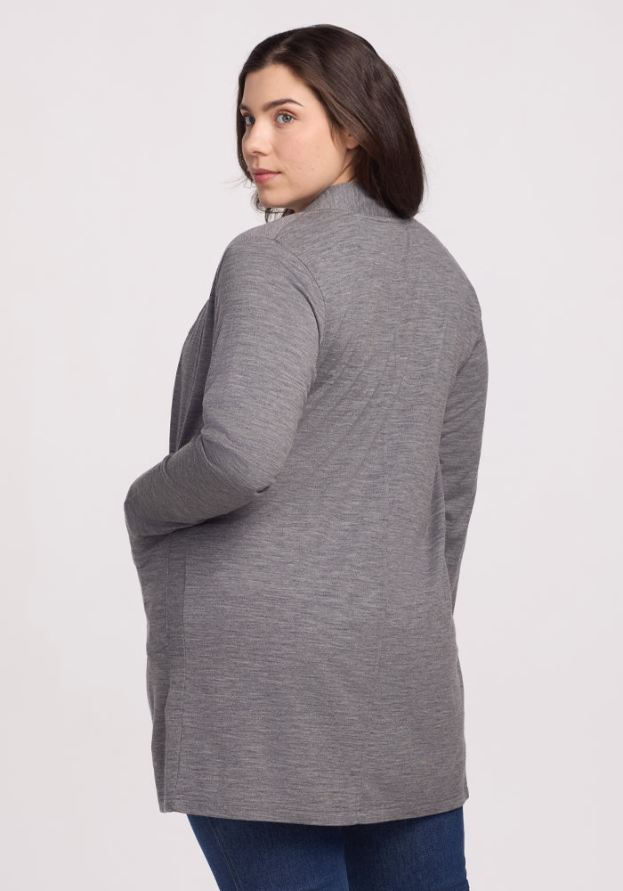 A woman with long dark hair, in blue jeans and a Woolx Paisley Cardigan in Graphite Heather, stands with her side and back visible. She looks to her left against a plain white background, exuding feather-light comfort.