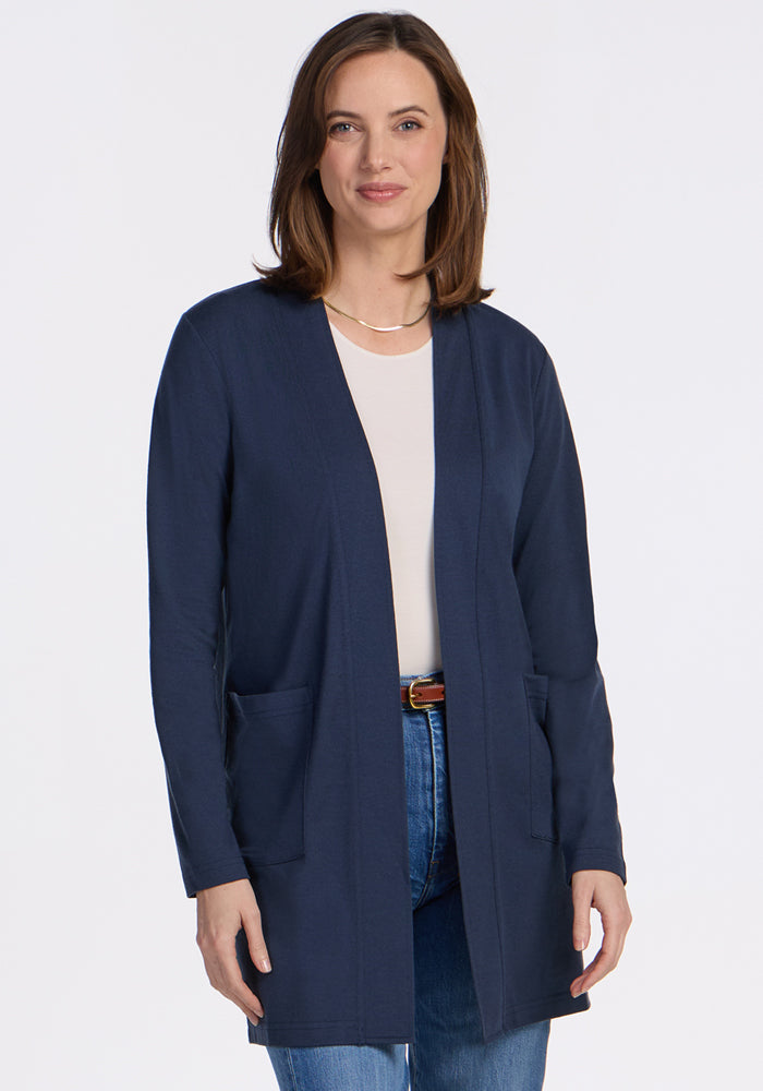 A woman with shoulder-length brown hair wears the Woolx Paisley Cardigan in Deep Navy over a white top and blue jeans, smiling against a plain white background—an essential piece for any wardrobe. | Jessica is 5’10”, wearing a size S