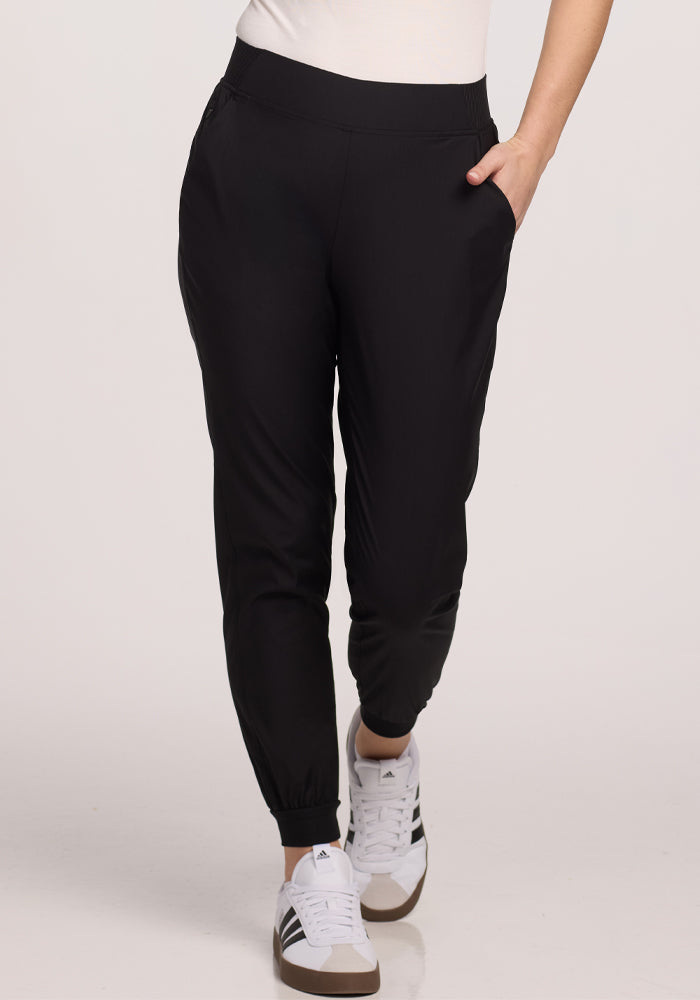 A person in Palmer Joggers - Black by Woolx, featuring deep pockets, pairs them with white sneakers adorned with black stripes, standing against a plain off-white background.