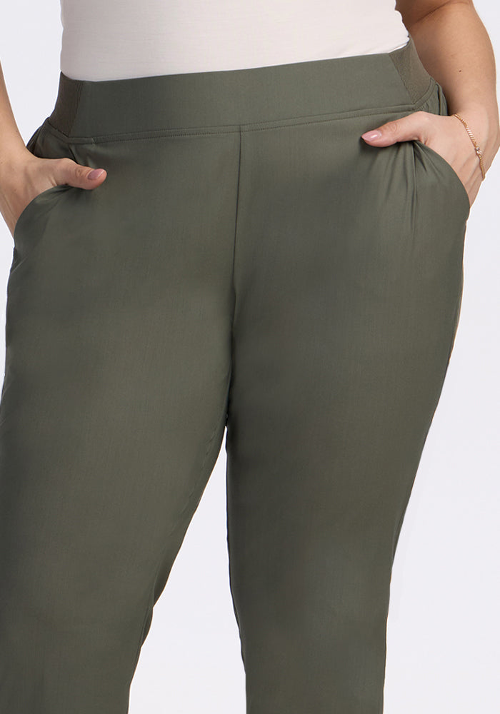 A person wearing Woolx Palmer Joggers - Sage Olive with hands in pockets, shown waist to mid-thigh. These joggers feature an elastic waistband and relaxed fit, ideal for comfortable movement while traveling.