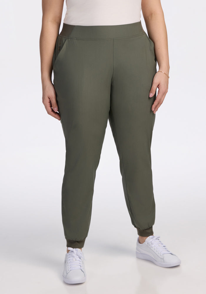 A person models the Woolx Palmer Joggers in Sage Olive with a white top and sneakers against a plain white background, showing only the lower half of their body. | Juliana is 5'10", wearing a size XL