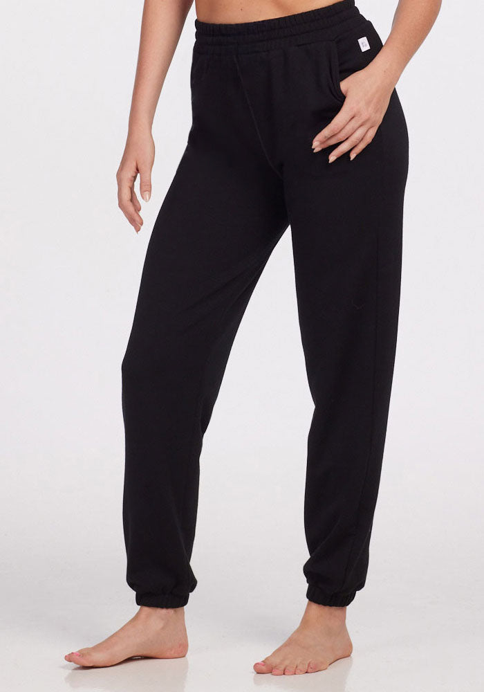 A person is wearing Woolx Parker Sweatpants - Black, featuring a relaxed fit, elastic waistband and cuffs, and moisture-wicking Merino wool, while standing barefoot against a plain white background. | Karly is 5'10", wearing a size S
