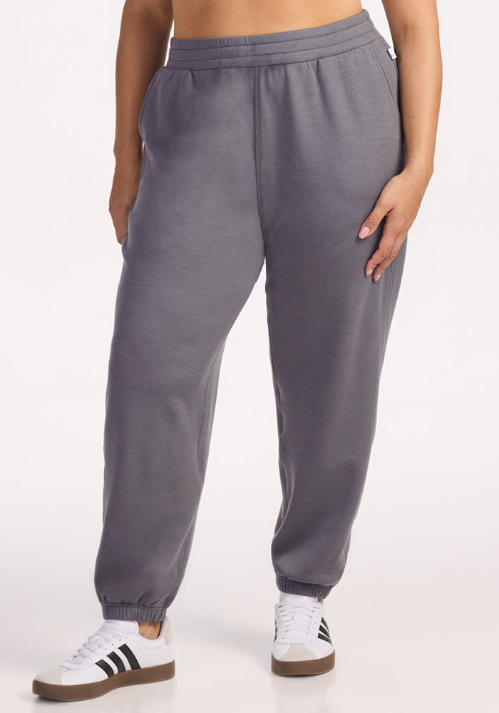 A person wears Woolx Parker Sweatpants in Arctic Dusk, standing against a plain white background. Only the lower torso and legs, paired with white sneakers with black stripes, are visible.