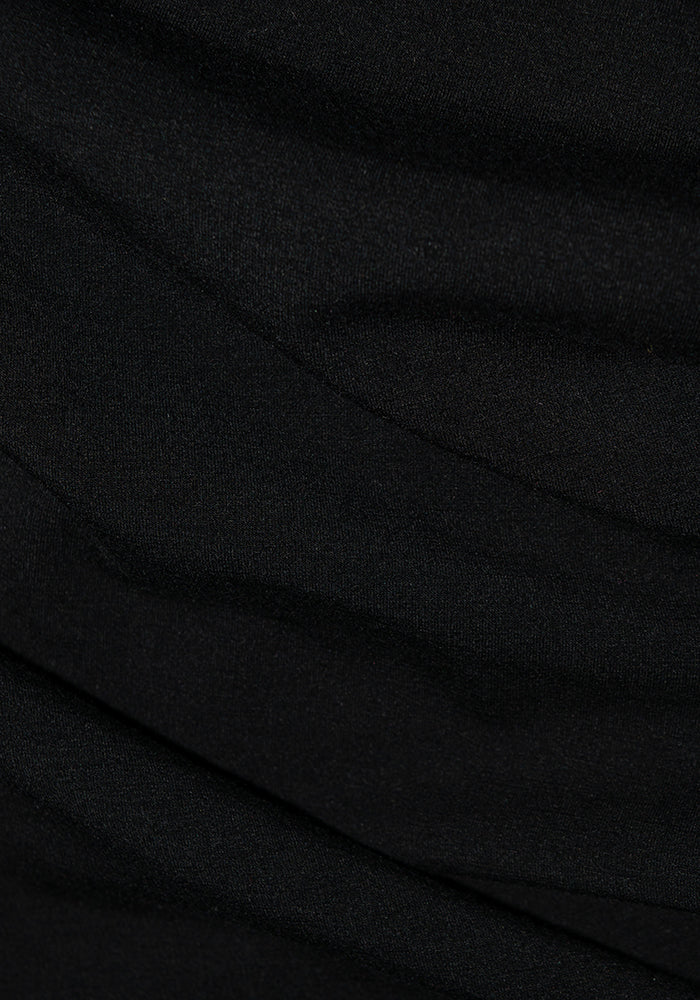 A close-up of the Piper Pocket Leggings in black, featuring a textured fabric that forms soft folds and subtle shadows. The smooth, slightly shiny material of these Woolx leggings suggests a lightweight, moisture-wicking textile ideal for cold-weather baselayers with gentle draping.
