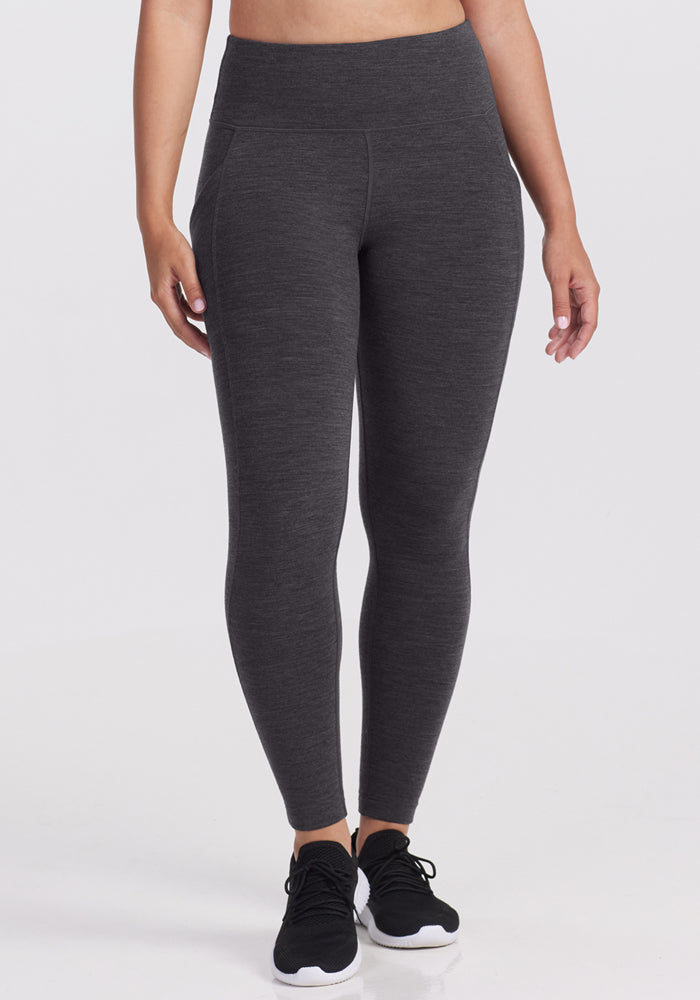 A person wearing Woolx Piper Pocket Leggings in Cinder Melange and black athletic shoes stands against a plain white background, shown from midriff to feet. | Tori is 5'7", wearing a size S