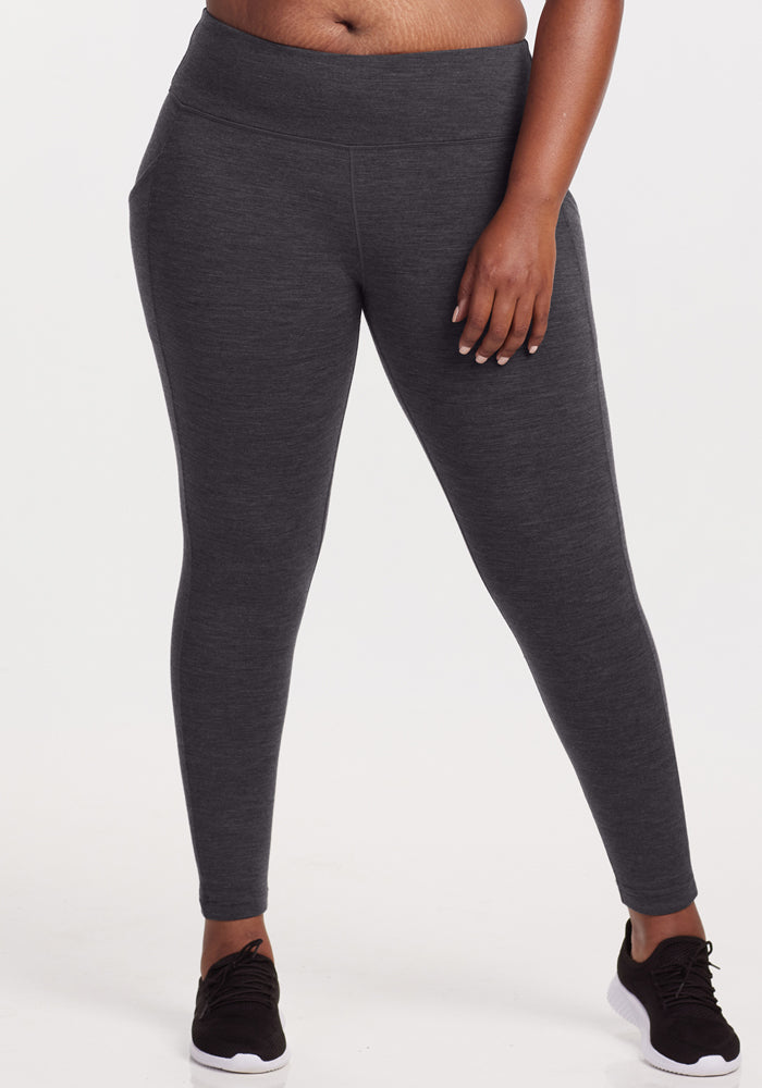 A person wears Woolx Piper Pocket Leggings in Cinder Melange with black sneakers, standing against a white background. The image is cropped from the chest down to highlight the fit of these women's Merino wool baselayer leggings. | Le'Quita is 5'11", wearing a size XL