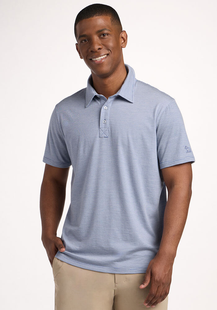 Smiling man in a Woolx Preston Polo - Blue Sand Mini Stripe, one hand in pocket, against a plain background. | Trell is 6’2”, wearing a size M
