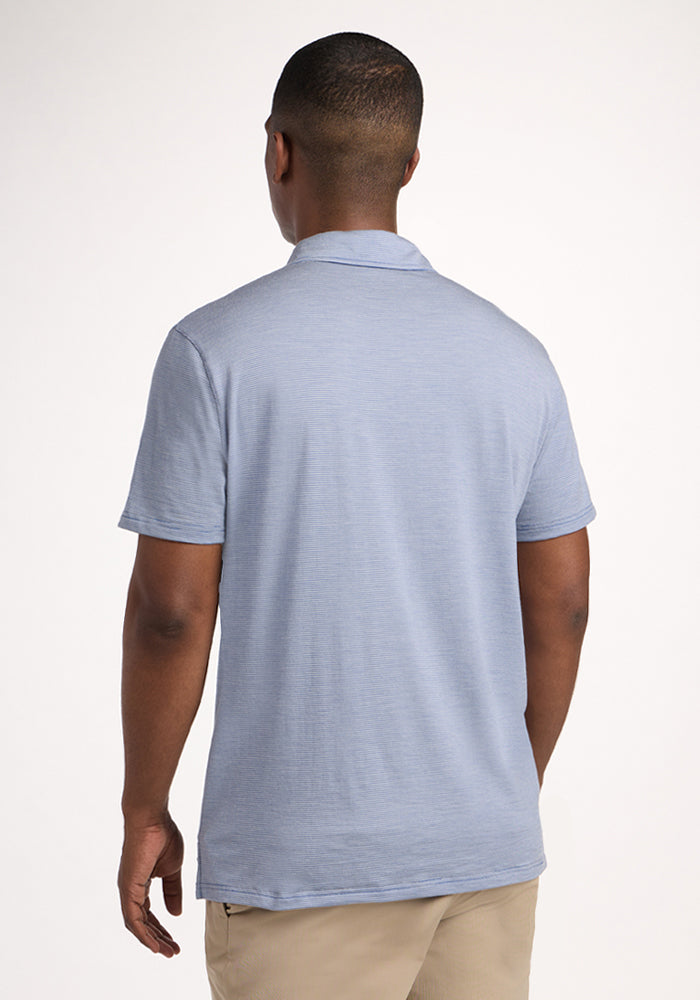 A man stands with his back to the camera, wearing the Woolx Preston Polo - Blue Sand Mini Stripe and beige pants, set against a plain light background.