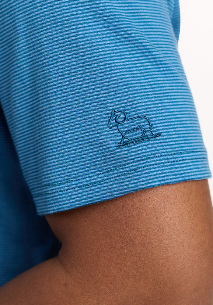 Close-up of a person's arm wearing the Woolx Preston Polo - Coastal Mini Stripe, a blue short-sleeve merino wool polo featuring thin stripes and a small embroidered ram outline on the sleeve.