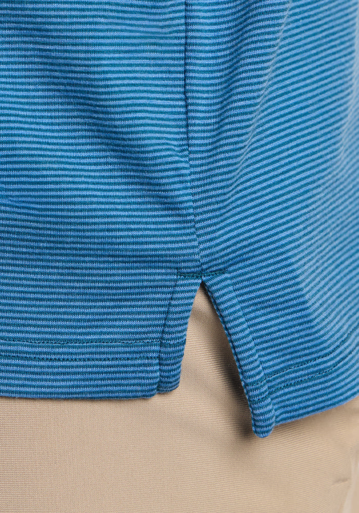 Close-up of the hem of the blue, ribbed Woolx Preston Polo - Coastal Mini Stripe with a small side slit, made from merino wool and worn over beige pants.