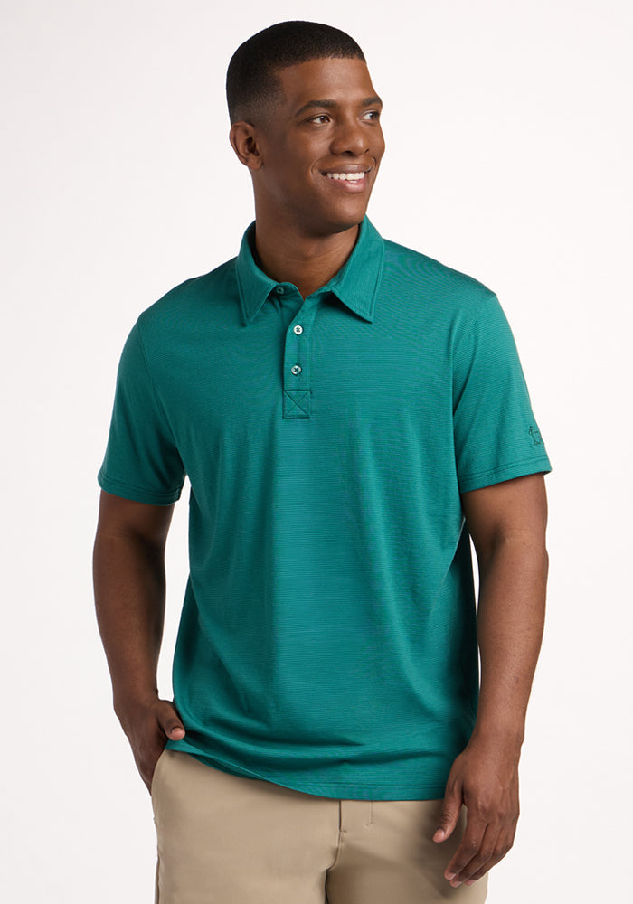 A man wearing a Woolx Preston Polo - Woodland Mini Stripe short-sleeve shirt and beige pants stands with his hands in his pockets, smiling and looking to the side against a plain white background.