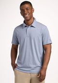 Smiling man in a Woolx Preston Polo - Blue Sand Mini Stripe, one hand in pocket, against a plain background. | Trell is 6’2”, wearing a size M