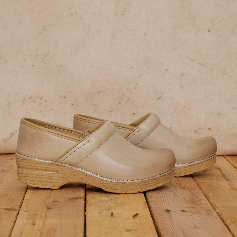 Sand-colored clogs shown in a wooden setting to match detail on outsoles.