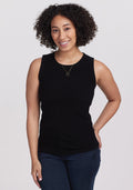 A person with curly hair wearing a Woolx Raegan Ribbed Tank Top in black and blue jeans smiles while standing against a plain background. | Tori is 5'7", wearing a size S