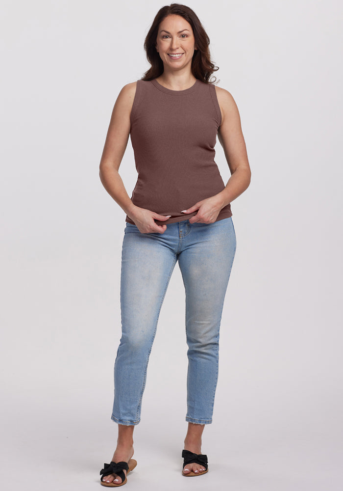 Woman smiling in the Woolx Raegan Ribbed Tank Top in Peppercorn, light blue jeans, and black sandals against a plain background.