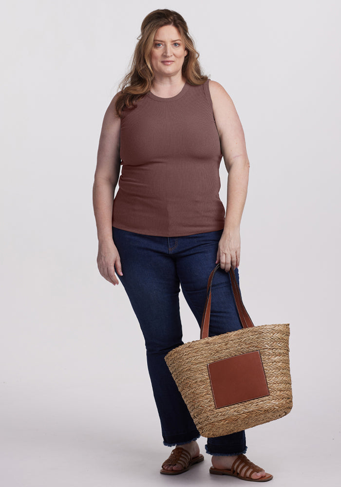 Woman with wavy brown hair in a Woolx Raegan Ribbed Tank Top - Peppercorn, blue jeans, sandals, holding a tote bag.