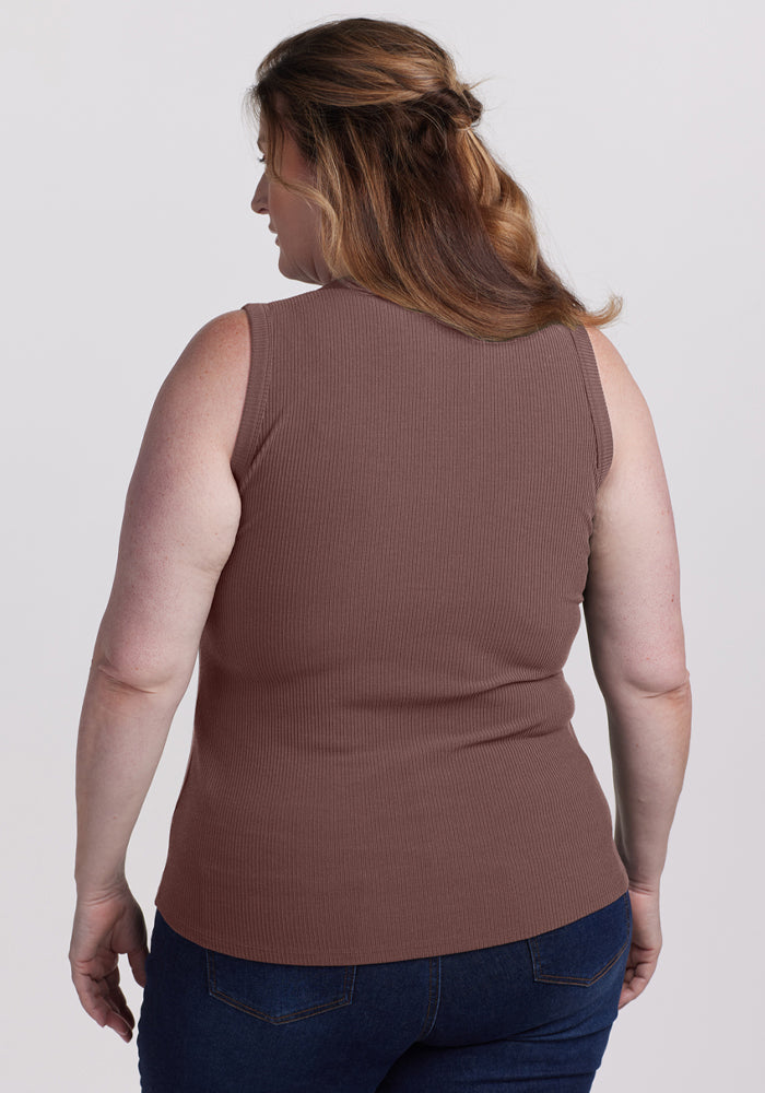 A woman with light brown hair faces away, wearing the Woolx Raegan Ribbed Tank Top - Peppercorn and dark blue jeans.
