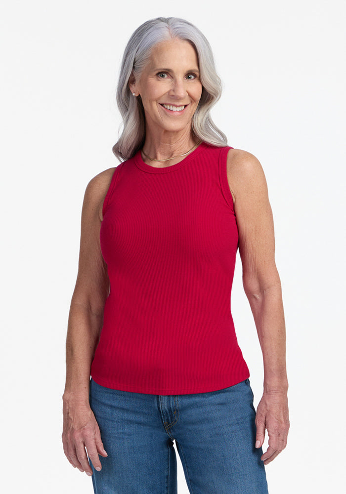Smiling older woman in a Woolx Raegan Ribbed Tank Top in Poppy Spark and blue jeans, against a plain background.