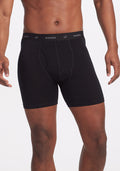 The image features an individual wearing the Reaction Boxer Briefs in Black, showcasing the Woolx brand name on the waistband. The front view highlights the comfortable fit of these performance boxers on the torso and upper legs. | Trell is 6’2”, wearing a size M