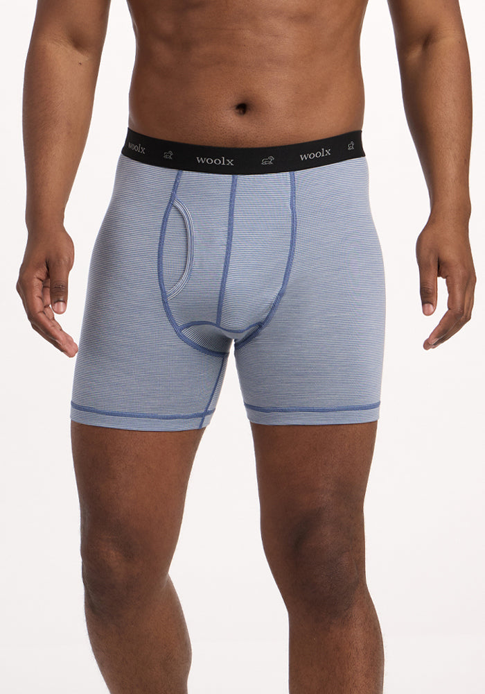 A person wears Woolx Reaction Boxer Briefs - Blue Sand Mini Stripe, featuring a black "Woolx" waistband, standing against a white background. Only the torso and upper legs are shown, highlighting this comfortable underwear. | Trell is 6’2”, wearing a size M
