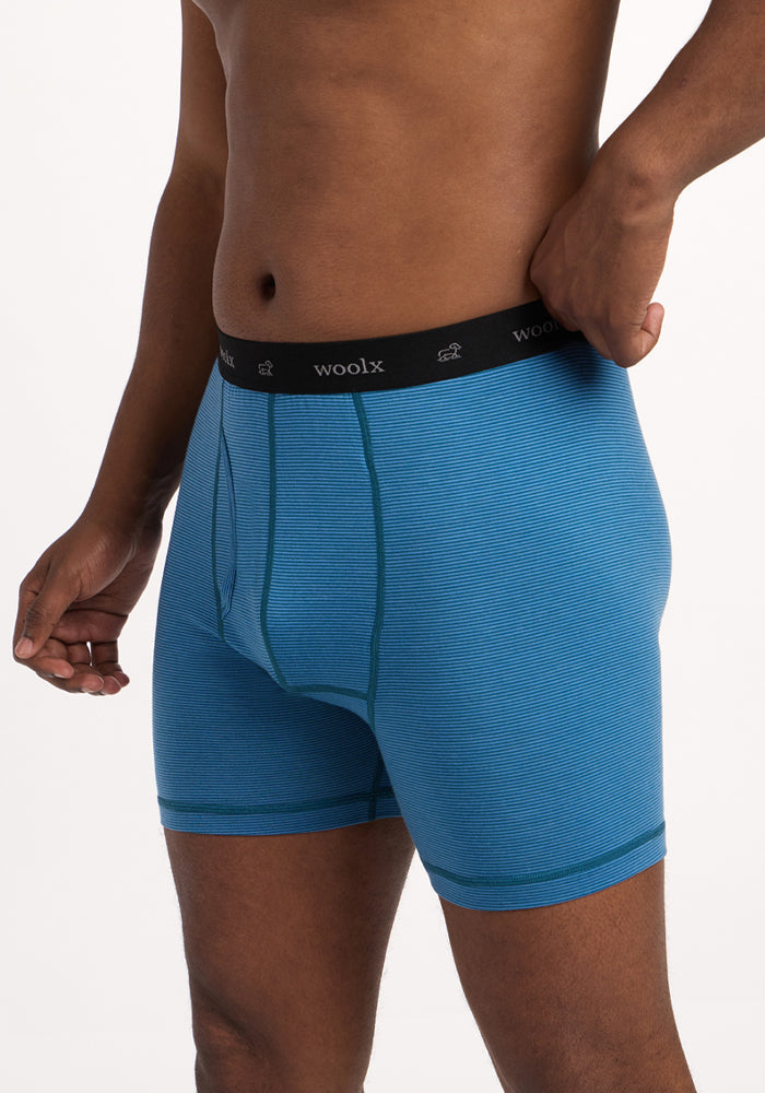 A person wears Woolx Reaction Boxer Briefs in Coastal Mini Stripe, featuring a black "woolx" waistband. Posed against a plain white background, only their torso and upper legs are visible.