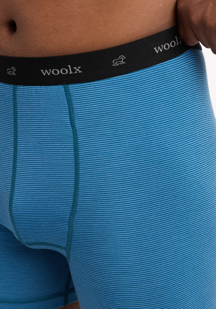 Close-up of a person wearing Woolx Reaction Boxer Briefs - Coastal Mini Stripe, featuring a black waistband with "woolx" and sheep icons in white. These boxer briefs are made from comfortable merino wool for top performance.
