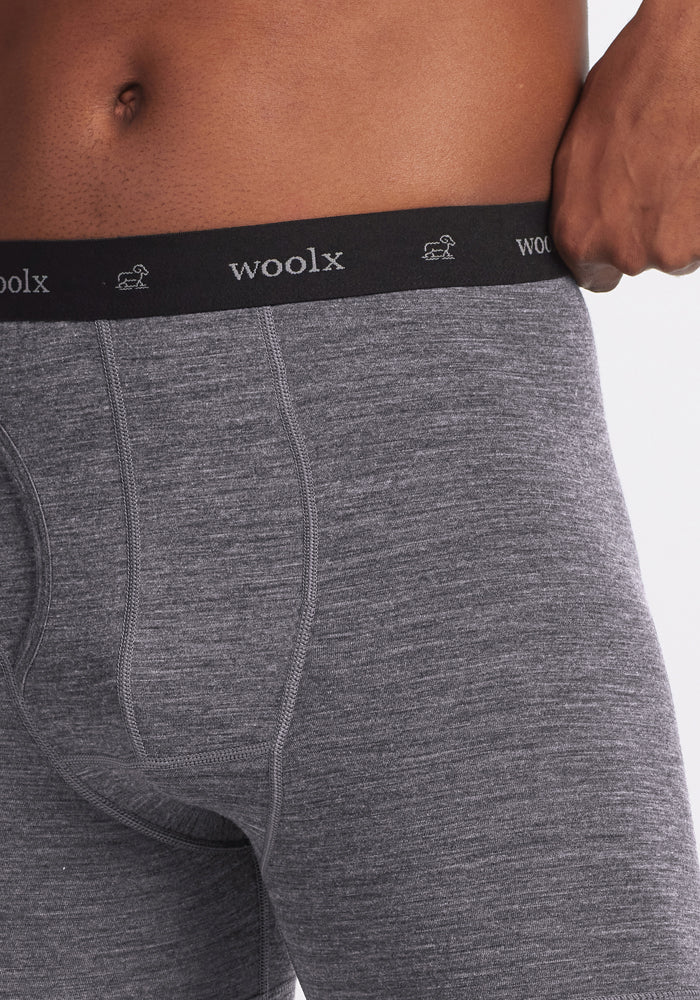 Close-up of someone wearing Woolx Reaction Boxer Briefs in Graphite Heather, featuring a black waistband with the Woolx logo and sheep icons, adjusting the comfortable Merino wool underwear with their right hand.